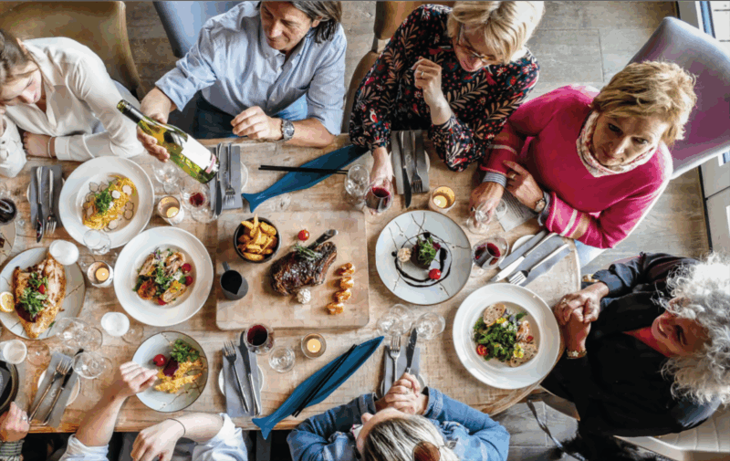 Eine Gruppe Menschen sitzen am Tisch und genießen eine lange Tafel aus Speisen und Getränken im Restaurant Coast auf Sylt